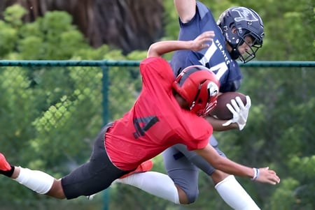 Un jugador de fútbol con camiseta roja atrapa el balón en el campo de la Saint Edward's School.