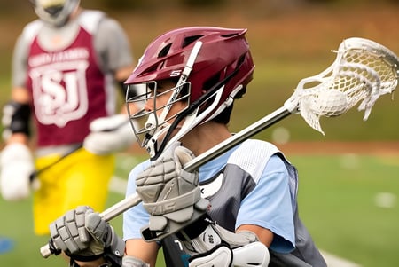 Un jugador de lacrosse de la Saint James School está de pie con casco y palo en el campo.