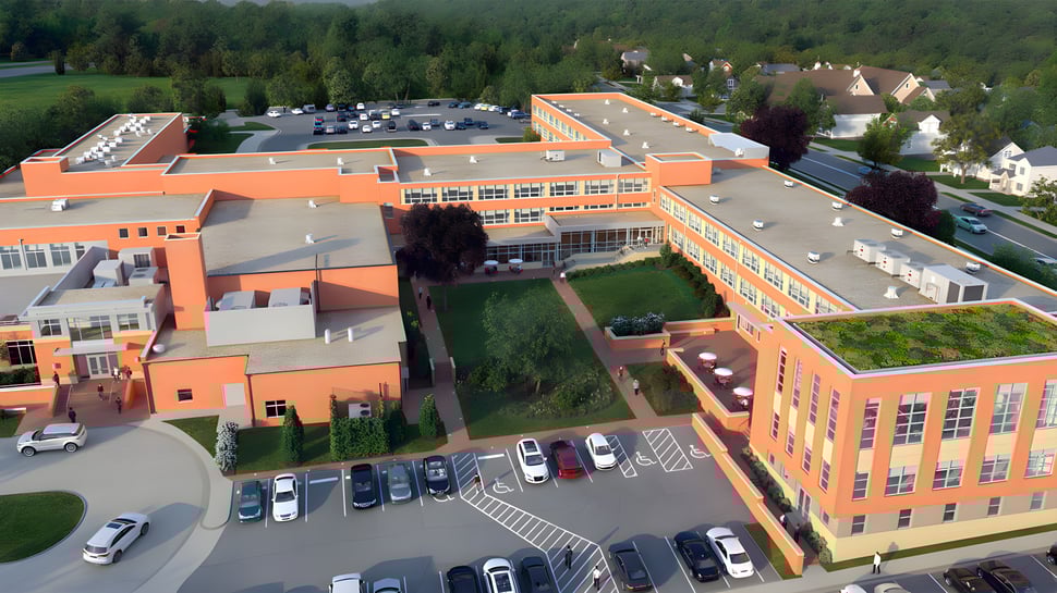 El edificio de varios pisos de la Saint Johns High School con techo naranja se encuentra en un estacionamiento frente a un fondo boscoso.
