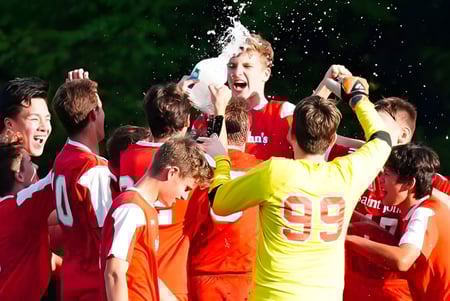 Los estudiantes de Saint John‘s Prep celebran juntos en un evento deportivo al aire libre con agua y un entorno verde.