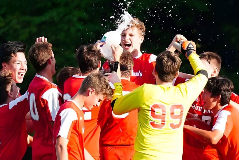 Los estudiantes de Saint John‘s Prep celebran juntos en un evento deportivo al aire libre con agua y un entorno verde.