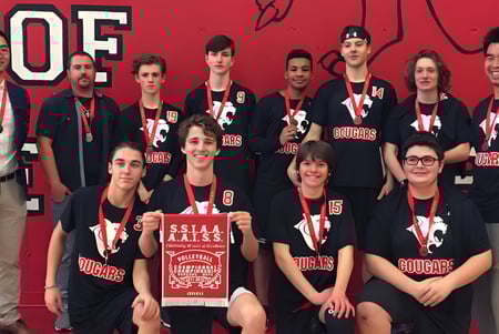 Un grupo de estudiantes posa frente a un fondo rojo con el logo de la Saint-Lambert International High School.