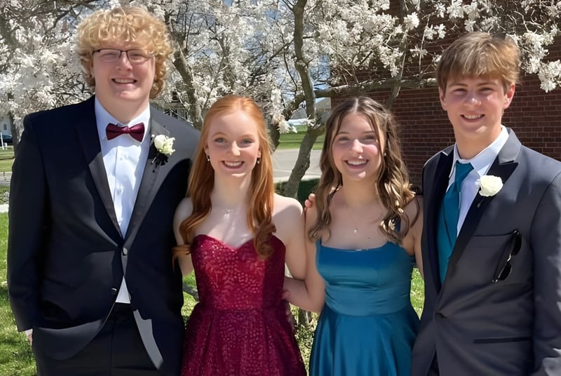 Cuatro estudiantes de la Saint Paul Lutheran High School están juntos en ropa formal en un parque con árboles en flor.