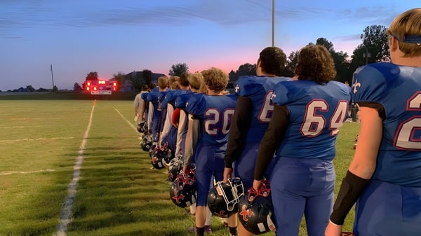 Un grupo de futbolistas con camisetas azules está en el campo de fútbol de la Saint Paul Lutheran High School al atardecer.