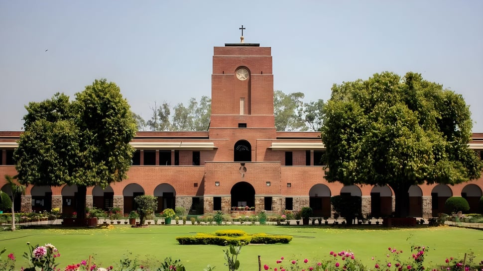 El edificio de ladrillo con una alta torre y una cruz en el campus del Saint Stephen’s College está rodeado de árboles verdes y cuidados parterres de flores.
