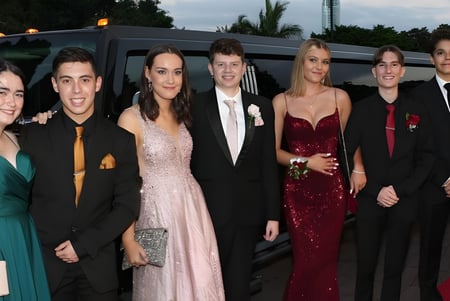 Un grupo de estudiantes bien vestidos del Saint Stephen’s College posan frente a una limusina en un evento escolar.