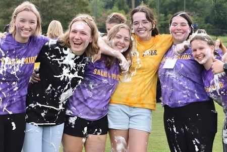 Un grupo de alumnas de la Salem Academy se abraza afuera frente a árboles y áreas verdes.