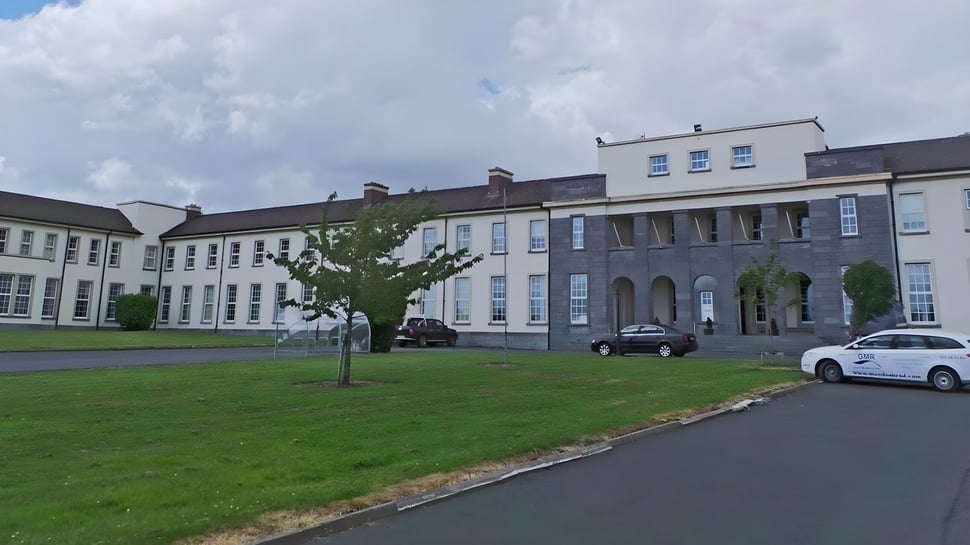 El edificio de varios pisos de la Salerno Secondary School con un área de césped en primer plano y vehículos estacionados en la calle.