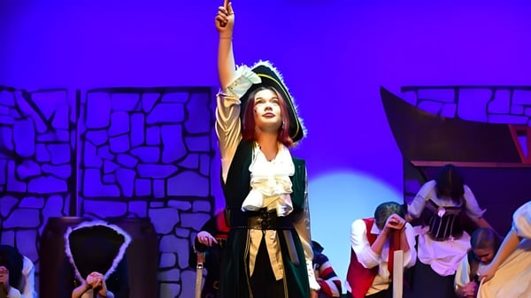 Una mujer en un disfraz está de pie con los brazos en alto en el escenario durante una actuación de la Salisbury High School.