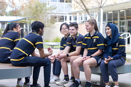 Estudiantes de la Salisbury High School están sentados juntos en un banco al aire libre frente a árboles y edificios.