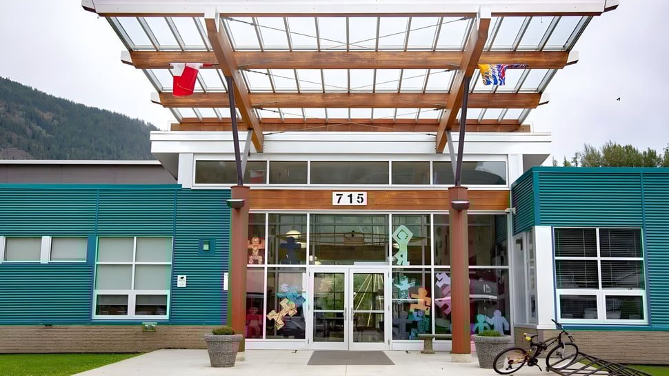 El moderno edificio de varios pisos de la Salmo Secondary School, con estructura de madera y paredes de vidrio, está rodeado de un área verde.