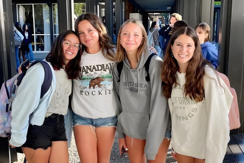 Un grupo de estudiantes posa frente a un edificio con grandes ventanas en el campus de la San Domenico School.