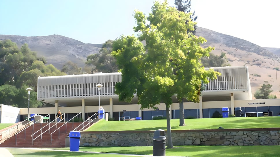 El moderno edificio de la San Luis Obispo High School con un prado y árboles en primer plano frente a un paisaje montañoso.