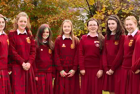 Un grupo de alumnas y alumnos del Sancta Maria College en uniformes escolares rojos se encuentra en el terreno otoñal con hojas de colores.
