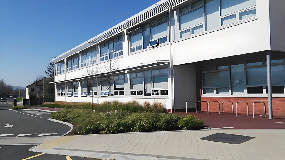 El moderno edificio de varios pisos del Sancta Maria College Ballyroan con grandes ventanas y un camino pavimentado en primer plano.