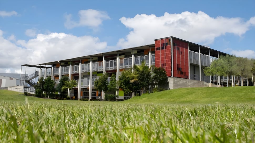 El moderno edificio del Sancta Maria College con fachada de vidrio y metal se encuentra en un campo cubierto de hierba bajo un cielo nublado.
