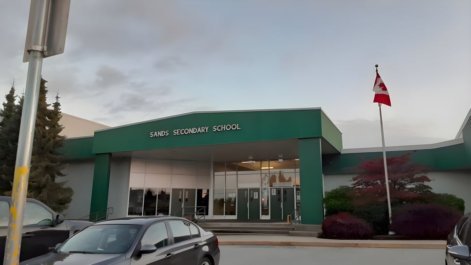 El edificio escolar pintado de verde de la Sands Secondary School con una bandera canadiense y árboles en el entorno.