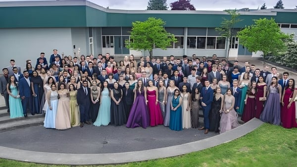 Un gran grupo de estudiantes en ropa formal se encuentra frente al edificio verde de la Sands Secondary School.