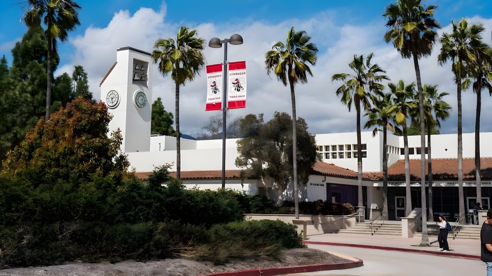 El edificio principal blanco con reloj en el campus del Santa Barbara City College está rodeado de palmeras y un camino.