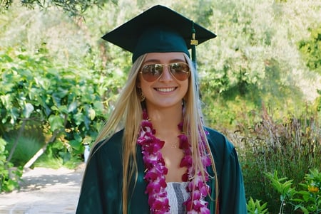 Una joven en vestimenta de graduación está en el área verde del campus del Santa Barbara Unified School District.