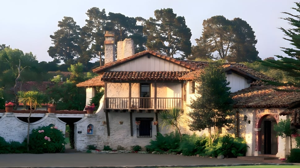 Una casa rústica con techo de tejas rodeada de exuberante vegetación y altos pinos en el terreno de la Santa Catalina School.