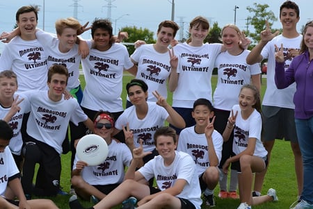 Un grupo de estudiantes de la Saunders Secondary School se reúne en un prado, algunos sentados, otros de pie.