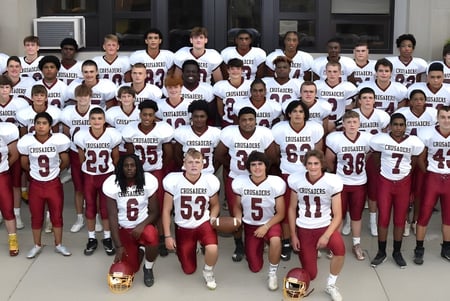 Un gran grupo de estudiantes atléticos de la Scecina Memorial High School está de pie en uniformes frente a un edificio.