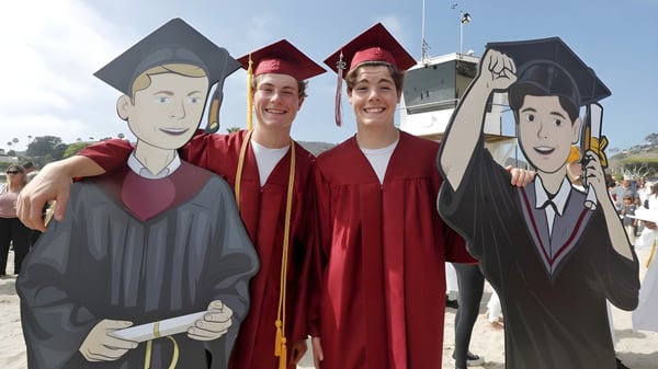 Tres estudiantes en ropa de graduación posan juntos frente a una pared con personajes de dibujos animados en el Schull Community College.