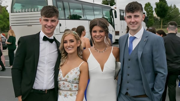 Cuatro alumnas y alumnos de Scoil Dara están frente a un autobús y posan para una foto grupal con ropa formal.
