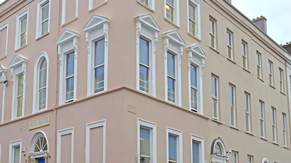 El edificio de varios pisos de la Scoil Mhuire Cork con grandes ventanas y fachada rosa en un entorno urbano.