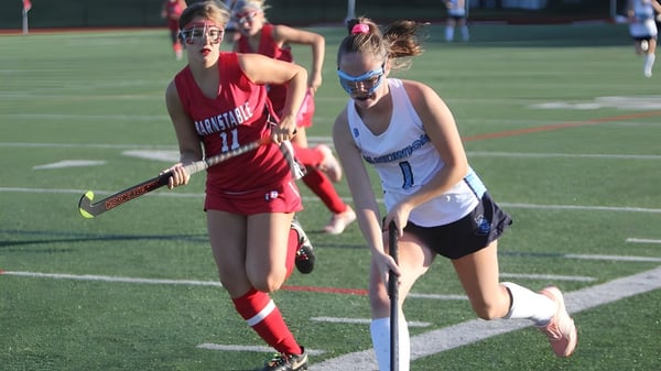 Dos estudiantes de la Scoil Mhuire Cork juegan un partido de hockey por la noche en el campo.