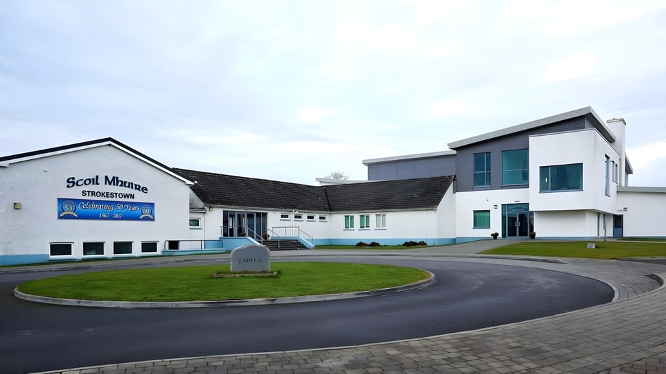 El moderno edificio de varios pisos de Scoil Mhuire (Strokestown) con una entrada curva y un área verde en primer plano.
