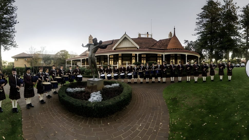 Un grupo de estudiantes en ropa formal está en el camino frente al edificio principal victoriano del Scotch College.