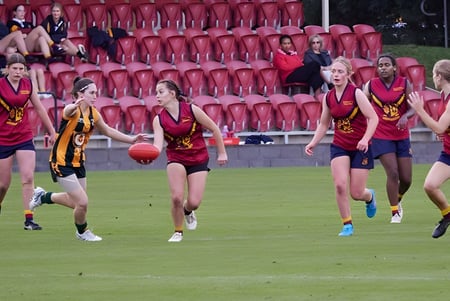 Un grupo de jóvenes deportistas juega en el campo de deportes del Scotch Oakburn College frente a espectadores.