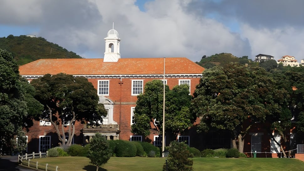 El edificio de ladrillo con torre campanario blanca en el terreno del Scots College está rodeado de mucho verde y árboles.
