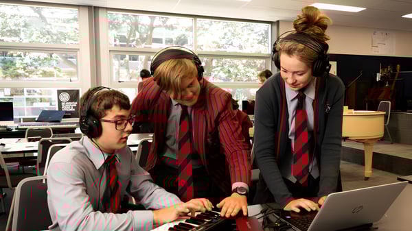 Estudiantes del Scots College trabajan juntos en una laptop en un aula con grandes ventanas.