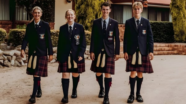 Cuatro estudiantes en uniformes escolares están de pie frente al edificio de ladrillo en el campus del Scots PGC College.