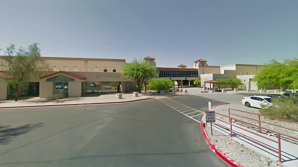 Un edificio escolar del Scottsdale Unified School District con estacionamiento y árboles en primer plano bajo un cielo azul claro.