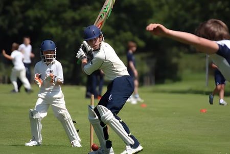 Un jugador de cricket del Seaford College golpea la pelota en el campo de césped con otros jugadores al fondo.