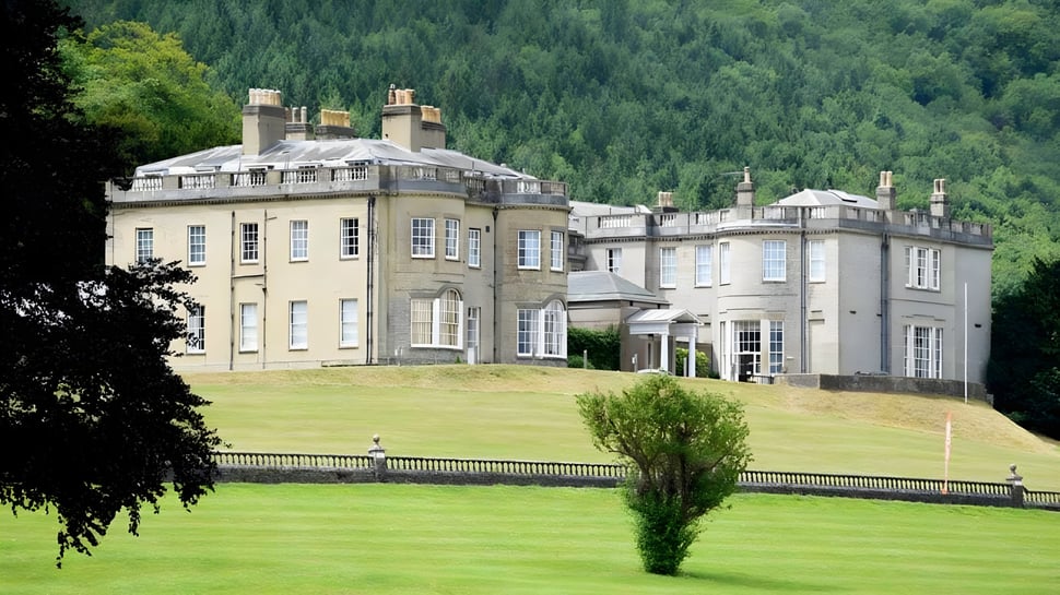 El edificio histórico del Seaford College se encuentra en una colina cubierta de hierba frente a un fondo boscoso.