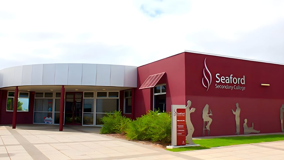 El moderno edificio rojo con el logo del Seaford Secondary College se encuentra en un terreno cubierto de hierba bajo un cielo nublado.