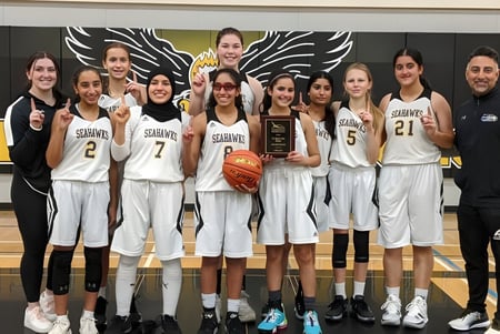 Un grupo de jugadoras de baloncesto de la Seaquam Secondary School sostiene un trofeo en el gimnasio.