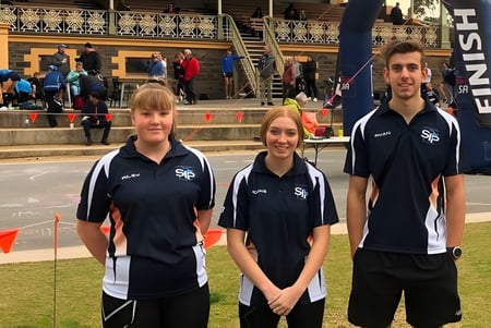 Tres estudiantes de la Seaton High School llevan uniformes deportivos y están frente a un edificio con fachada decorativa.