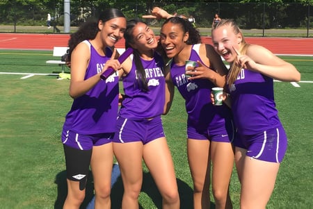 Un grupo de estudiantes en uniformes morados posan en el campo deportivo de Seattle Public Schools para una foto.