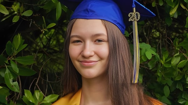 Una joven con birrete azul sonríe en el verde exterior del campus de Seattle Public Schools.