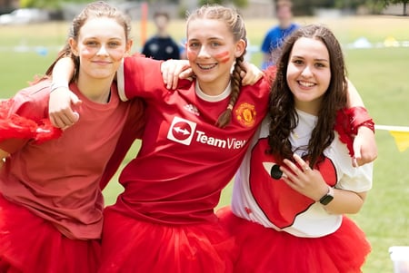 Tres estudiantes de la Seaview High School llevan camisetas rojas de Manchester United y se abrazan en un campo de césped.