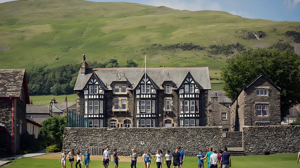 Un edificio Tudor histórico de la Sedbergh School con colinas verdes y montañas de fondo.