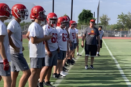 Un grupo de jóvenes jugadores de fútbol americano entrena con su entrenador en el campo de deportes de la Seton Catholic High School.