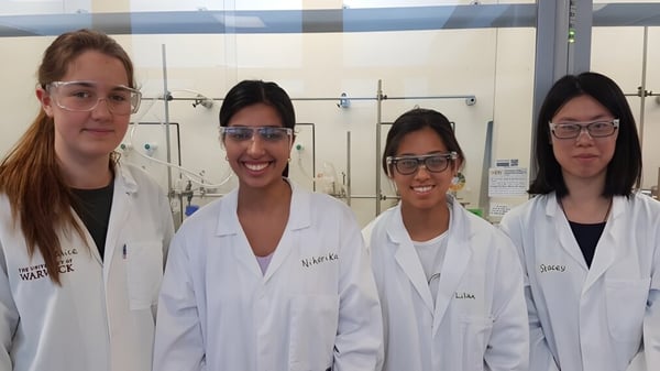 Cuatro estudiantes de la Sevenoaks School están en batas de laboratorio blancas en un laboratorio con equipos científicos.
