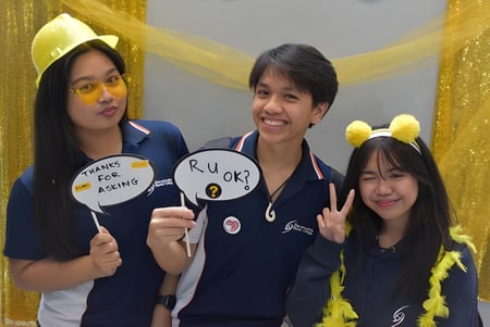 Tres estudiantes del Sevenoaks Senior College sostienen carteles en un marco colorido y festivo.